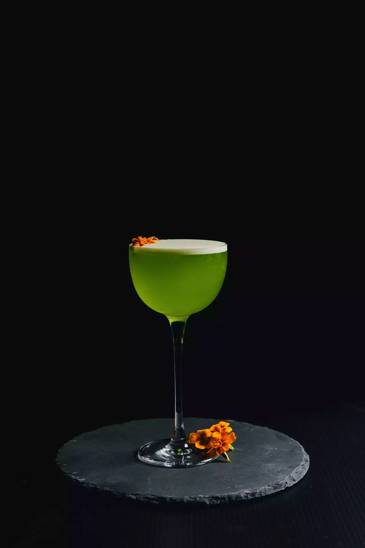 A green cocktail in a coupe on a black bar